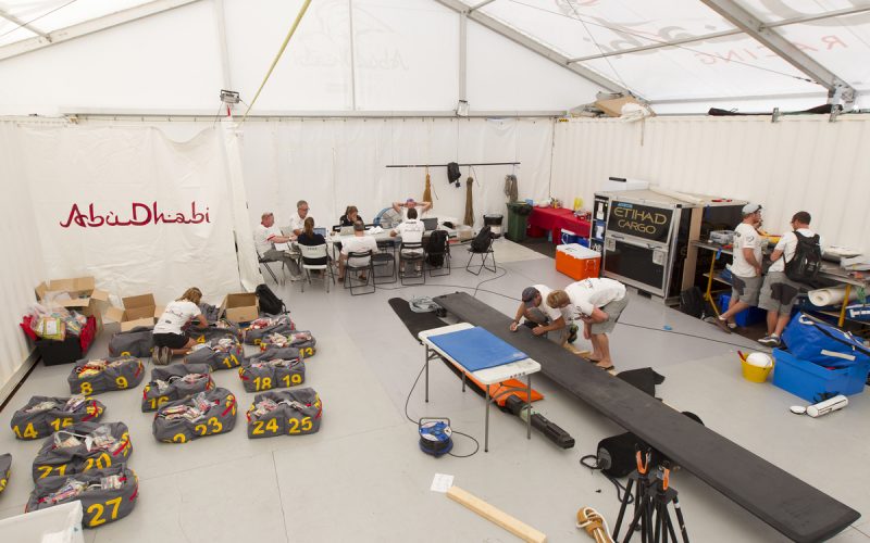 SOUTH AFRICA, Cape Town. 12th November 2014. Volvo Ocean Race. Abu Dhabi Ocean Racing team base. Multi function space, clockwise from the left, Alex Wardall, boat logistics, packs the food bags for Leg 2, planning meeting for the next few days, (table left), performance meeting, (table right), Sailing team undertake repairs (right) and shore crew maintain one of the dagger boards (centre).